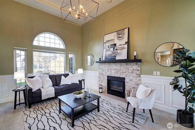 carpeted living room with a stone fireplace and a notable chandelier