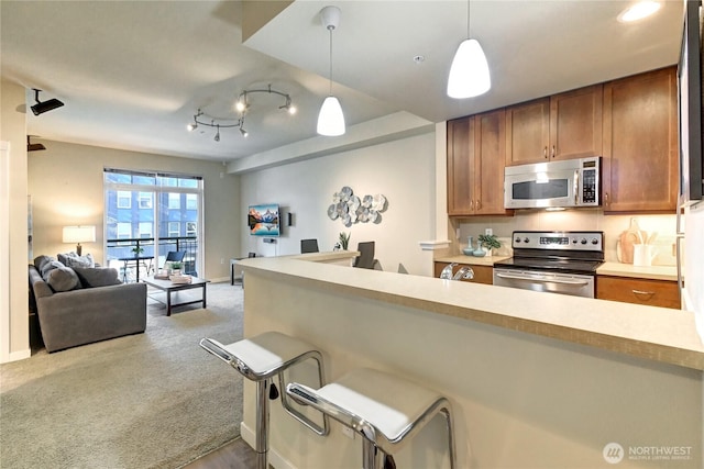 kitchen featuring decorative light fixtures, open floor plan, appliances with stainless steel finishes, and brown cabinets