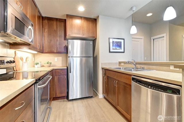 kitchen featuring decorative light fixtures, light countertops, brown cabinetry, stainless steel appliances, and a sink