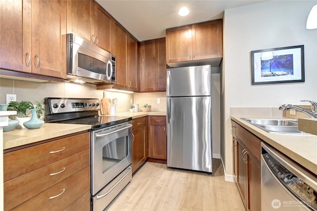 kitchen with a sink, light wood-style floors, appliances with stainless steel finishes, and light countertops