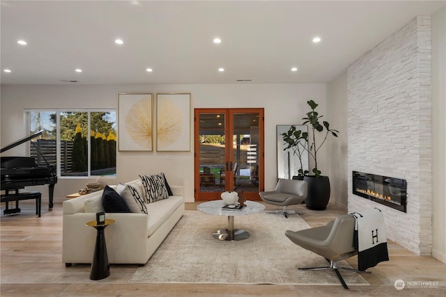 living room featuring a stone fireplace, light hardwood / wood-style floors, and french doors