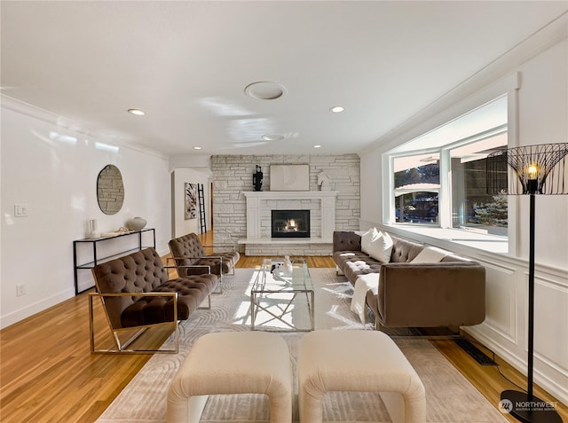 living room with baseboards, ornamental molding, a stone fireplace, light wood-type flooring, and recessed lighting