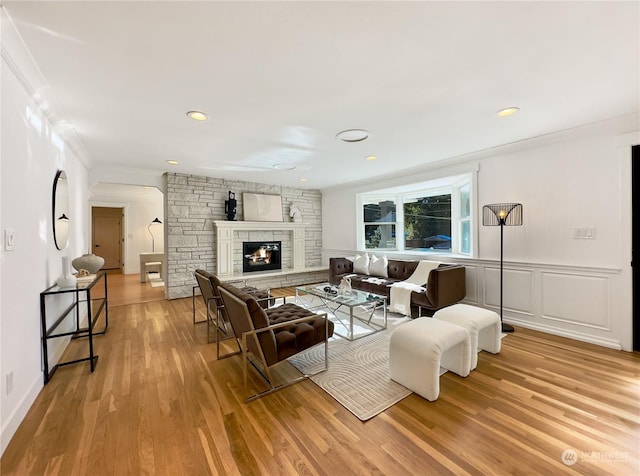 living room with light wood finished floors, a wainscoted wall, a stone fireplace, a decorative wall, and recessed lighting