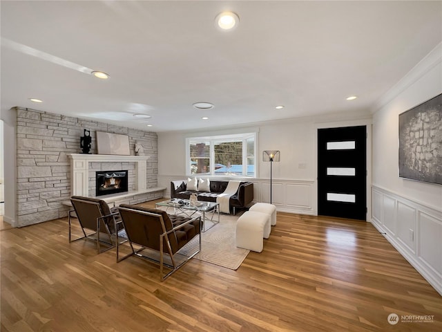 living room featuring a stone fireplace, wood finished floors, and a decorative wall