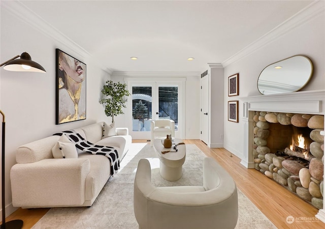 living area featuring baseboards, crown molding, french doors, light wood-type flooring, and a fireplace