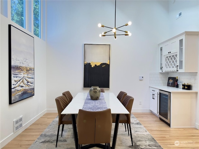 dining room featuring beverage cooler, a dry bar, visible vents, and light wood-style floors