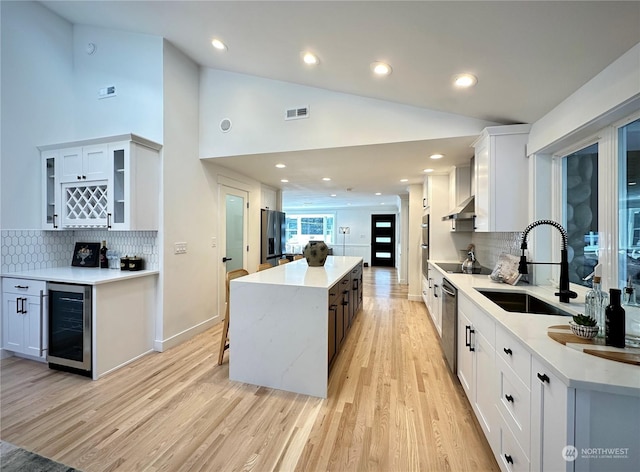 kitchen featuring appliances with stainless steel finishes, white cabinetry, a kitchen island, a sink, and beverage cooler