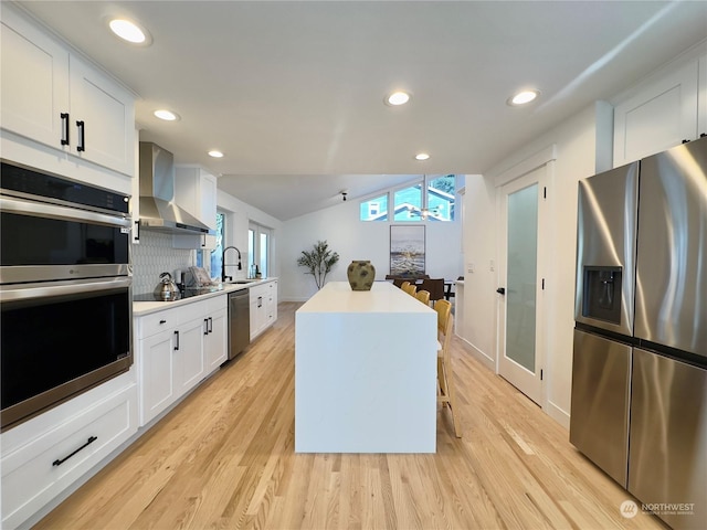 kitchen featuring stainless steel appliances, white cabinetry, light wood finished floors, and wall chimney exhaust hood