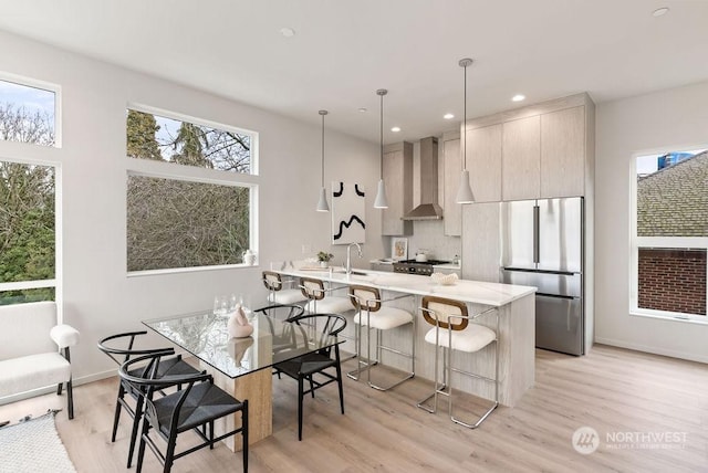 kitchen featuring wall chimney range hood, stainless steel refrigerator, a kitchen bar, decorative light fixtures, and kitchen peninsula