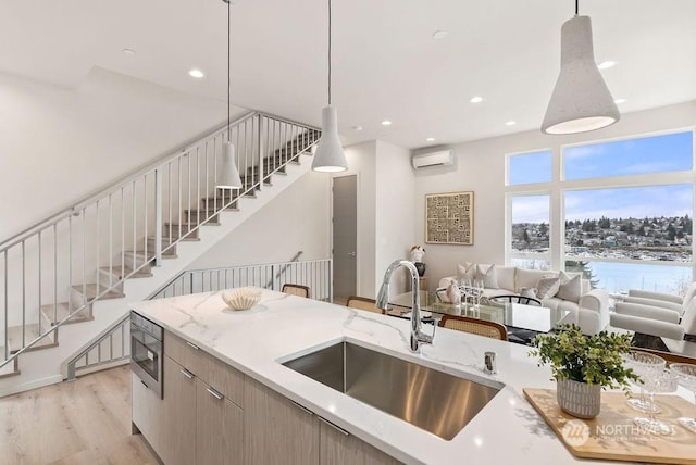 kitchen with sink, light stone counters, light hardwood / wood-style floors, decorative light fixtures, and an AC wall unit