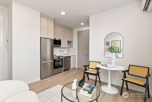 interior space with stainless steel appliances, sink, a wall mounted air conditioner, and light hardwood / wood-style flooring