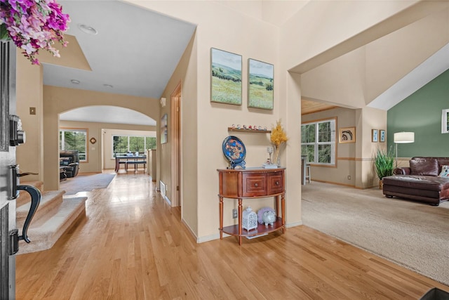 corridor with light wood-style floors, baseboards, and arched walkways