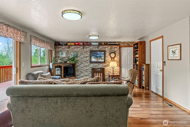 living area featuring light wood-style floors, visible vents, a textured ceiling, and baseboards