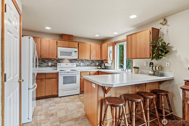 kitchen featuring a peninsula, white appliances, a sink, light countertops, and decorative backsplash