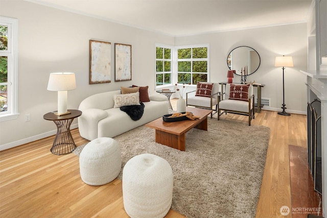 living area with baseboards, visible vents, a fireplace with flush hearth, wood finished floors, and crown molding