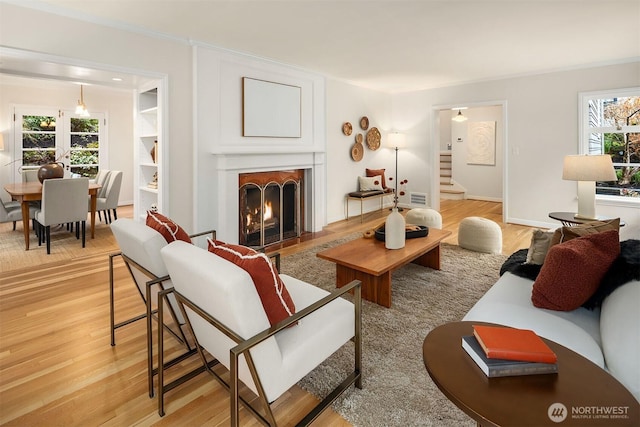 living room with a warm lit fireplace, visible vents, light wood-style flooring, and stairs