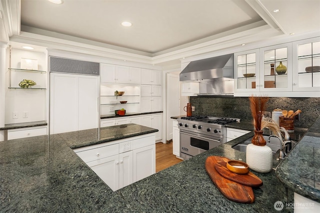 kitchen with white cabinets, high end appliances, glass insert cabinets, wall chimney range hood, and a sink