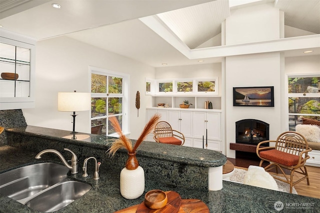 interior space with recessed lighting, a warm lit fireplace, vaulted ceiling, and wood finished floors