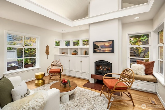 living area featuring a glass covered fireplace, visible vents, and light wood finished floors