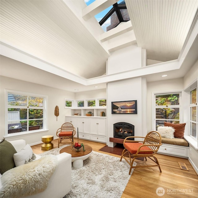 interior space featuring a skylight, visible vents, baseboards, light wood-style floors, and a glass covered fireplace