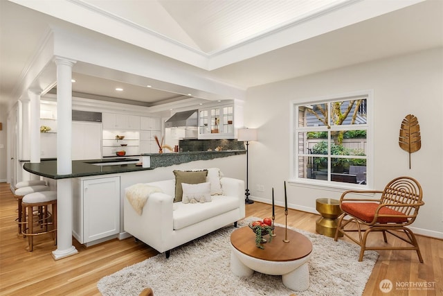 living area featuring lofted ceiling, ornate columns, baseboards, and light wood-style floors