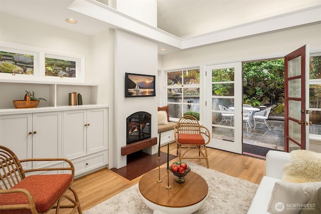 living area with a warm lit fireplace, french doors, light wood-style flooring, and recessed lighting