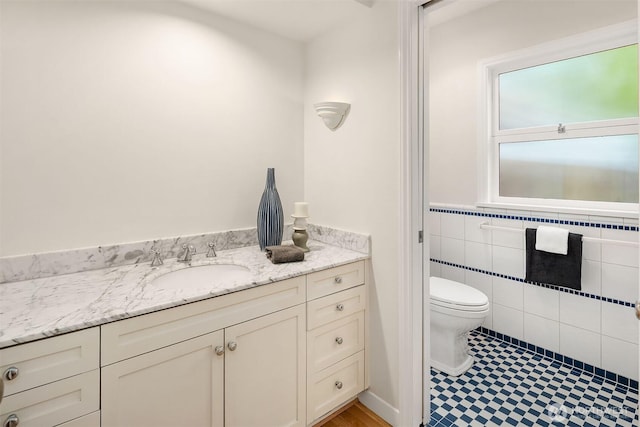 bathroom featuring a wainscoted wall, tile walls, toilet, and vanity