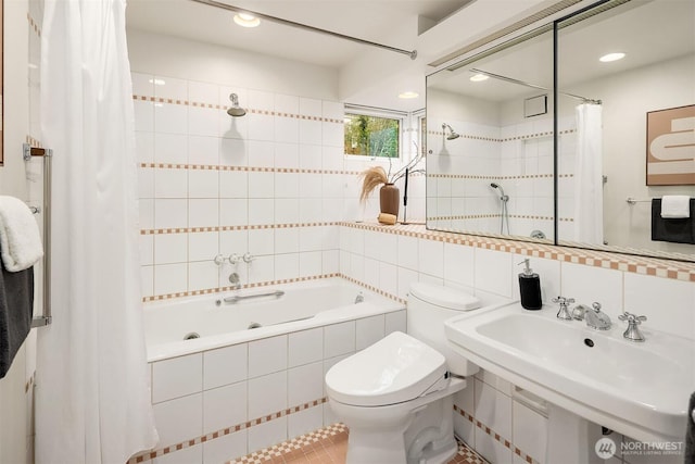 bathroom with tile walls, decorative backsplash, toilet, tiled shower / bath, and a sink