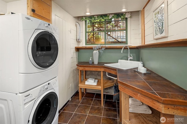 washroom with laundry area, dark tile patterned floors, a sink, and stacked washer and clothes dryer