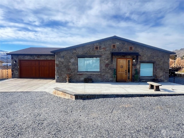 view of front of house featuring an attached garage, stone siding, fence, and concrete driveway