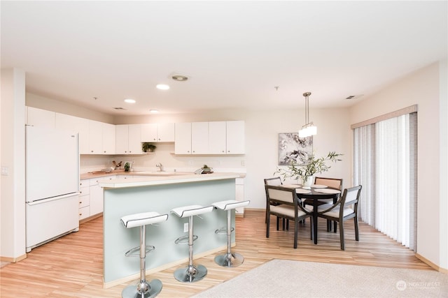 kitchen with decorative light fixtures, white cabinetry, white fridge, a center island, and light wood-type flooring