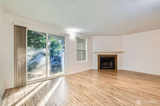 unfurnished living room with a tiled fireplace, a textured ceiling, and light wood-type flooring