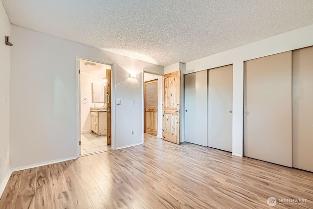 unfurnished bedroom with multiple closets, ensuite bathroom, a textured ceiling, and light wood-type flooring