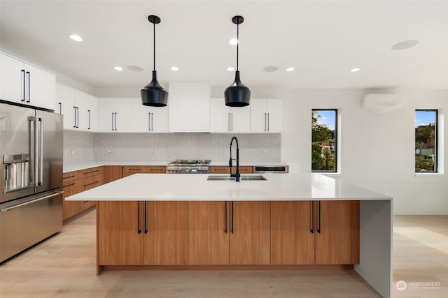 kitchen with high quality fridge, pendant lighting, sink, white cabinets, and a kitchen island with sink