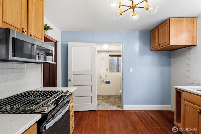 kitchen with appliances with stainless steel finishes, a notable chandelier, light stone countertops, backsplash, and dark hardwood / wood-style flooring