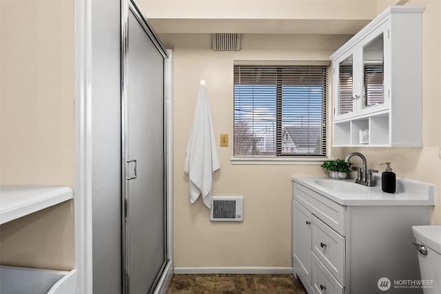 bathroom with heating unit, toilet, a shower with shower door, and vanity