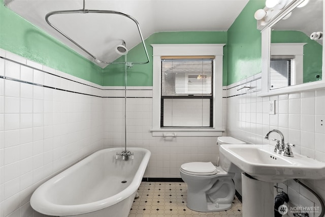 bathroom with a healthy amount of sunlight, a bathing tub, tile walls, and toilet