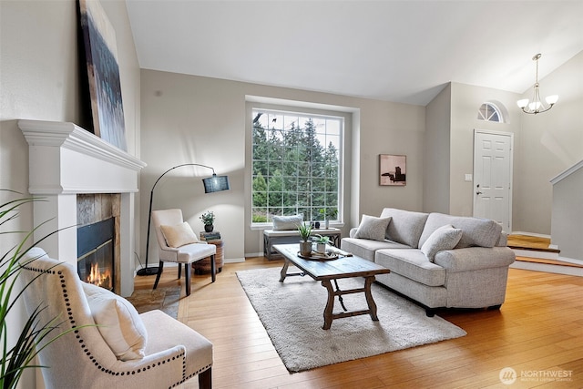 living room featuring a notable chandelier, a tiled fireplace, vaulted ceiling, and light wood-type flooring