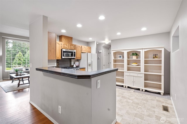 kitchen featuring white fridge with ice dispenser, range, and kitchen peninsula