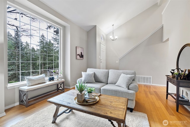 living room with a healthy amount of sunlight, lofted ceiling, light hardwood / wood-style floors, and a notable chandelier