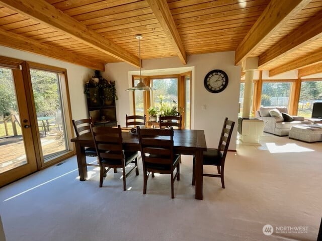 carpeted dining space with beam ceiling, a healthy amount of sunlight, and wood ceiling