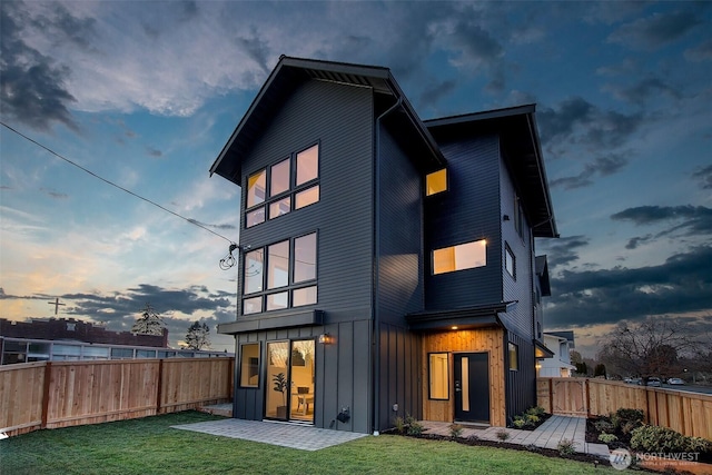 back house at dusk featuring a patio area and a lawn