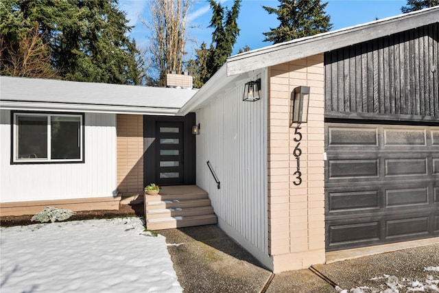 snow covered property entrance featuring a garage