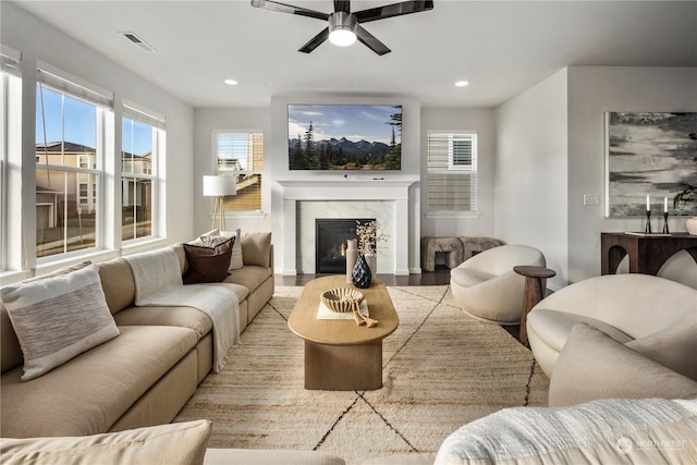 living room with a premium fireplace, ceiling fan, and light wood-type flooring