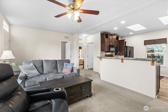 living area featuring a skylight, recessed lighting, visible vents, light carpet, and ceiling fan