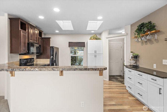 kitchen featuring white cabinets, dark brown cabinets, black appliances, light wood finished floors, and a kitchen bar