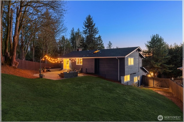 back house at dusk with a patio, outdoor lounge area, and a lawn