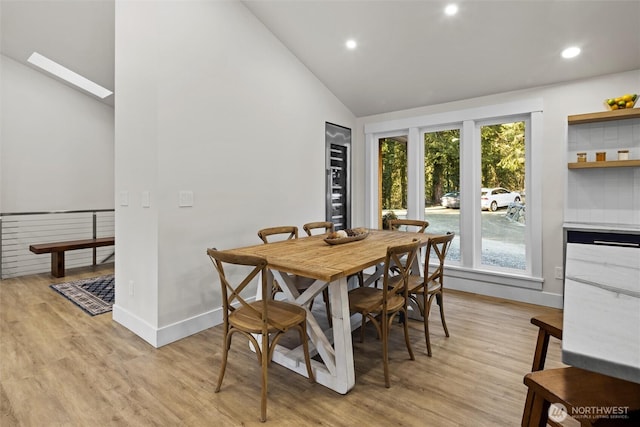 dining area with light hardwood / wood-style flooring, a skylight, and high vaulted ceiling