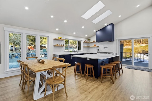 dining area featuring high vaulted ceiling, sink, a skylight, and light hardwood / wood-style floors