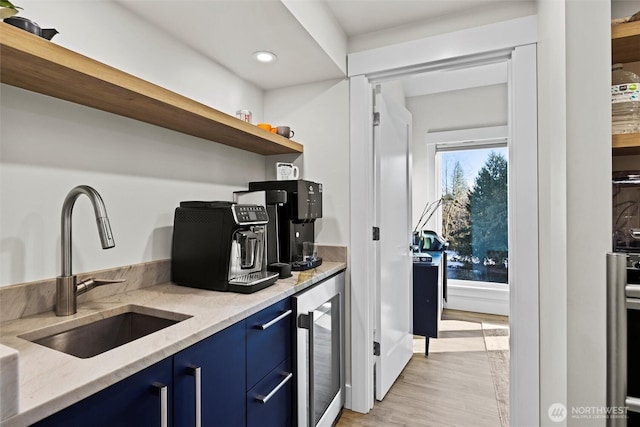 kitchen with wine cooler, blue cabinetry, sink, light stone countertops, and light hardwood / wood-style floors